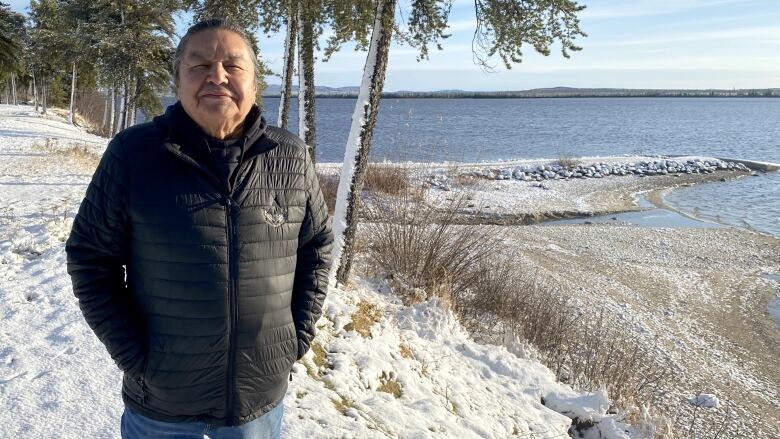 A man stands on a snowy shore in front of a lake. 