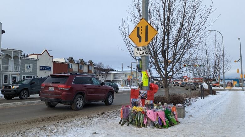 Flowers and posters commemorating Aaron Smarch lay alongside a snowy street while traffic drives by.