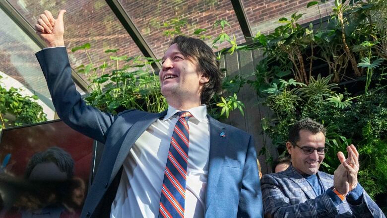 A man giving a thumbs up as people applaud around him. 