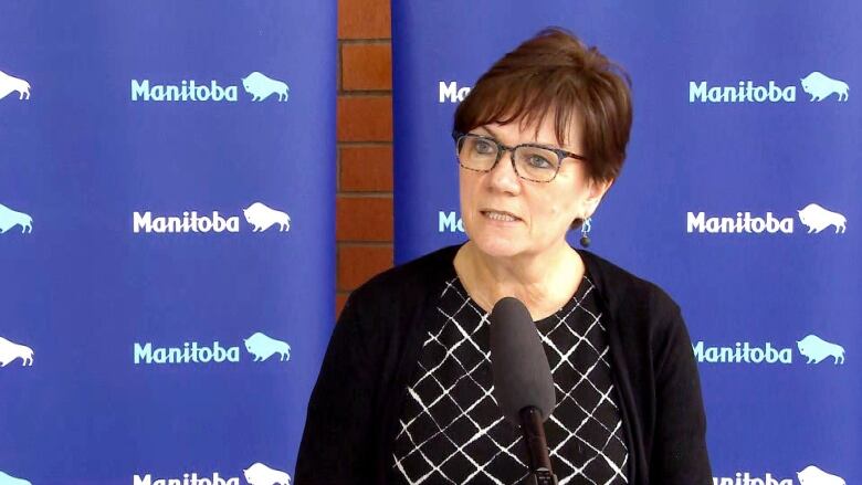 A lady stands and speaks into a microphone in front of a blue background.