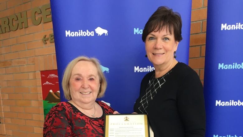 Two women stand with a declaration from the province of Manitoba.