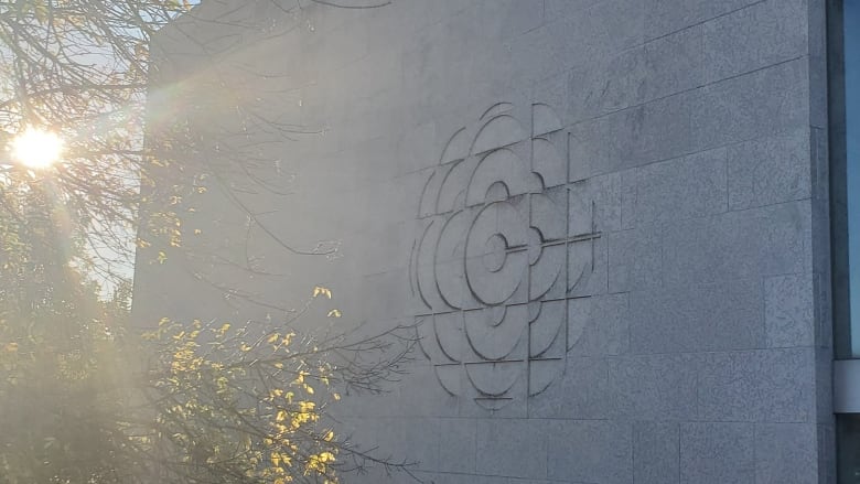 The sun shines on a giant CBC logo engraved into the Tyndall Stone of a building