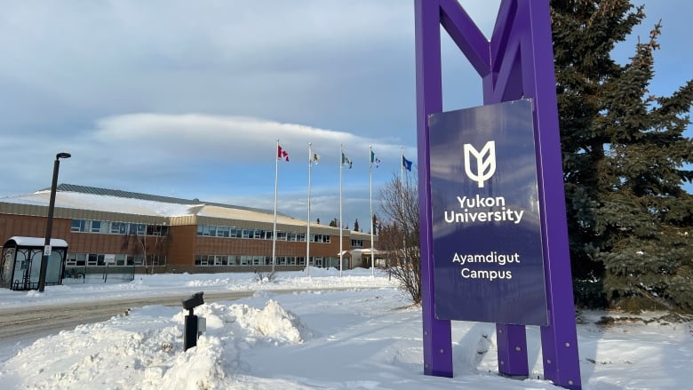 A sign reading, 'Yukon University Ayamdigut Campus' is seen in front of a building and a row of flags.