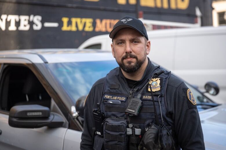 A police officer in full uniform smiles in front of a silver car.