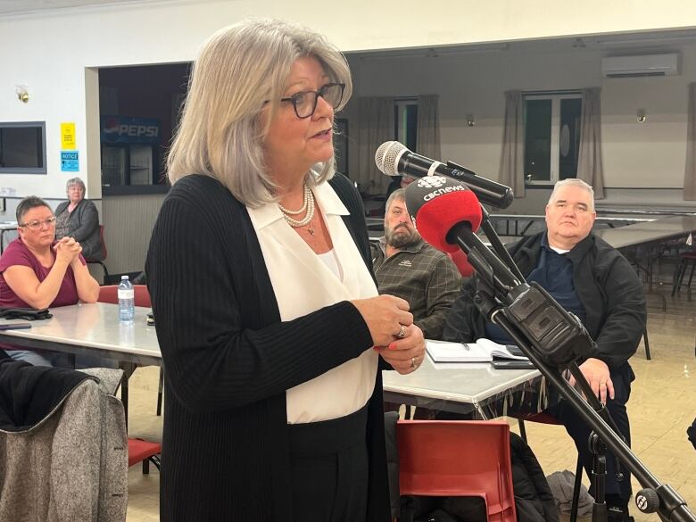 A woman stands at a mike during a public meeting 