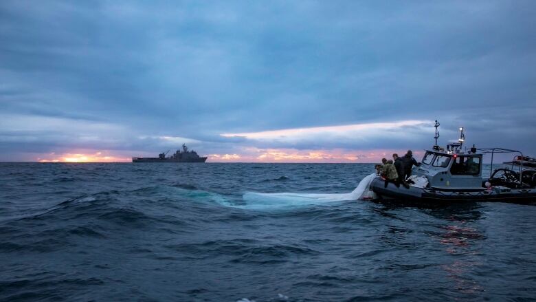 Daybreak shot of two boats on the water, with one boat's crew pulling the white material out of the water