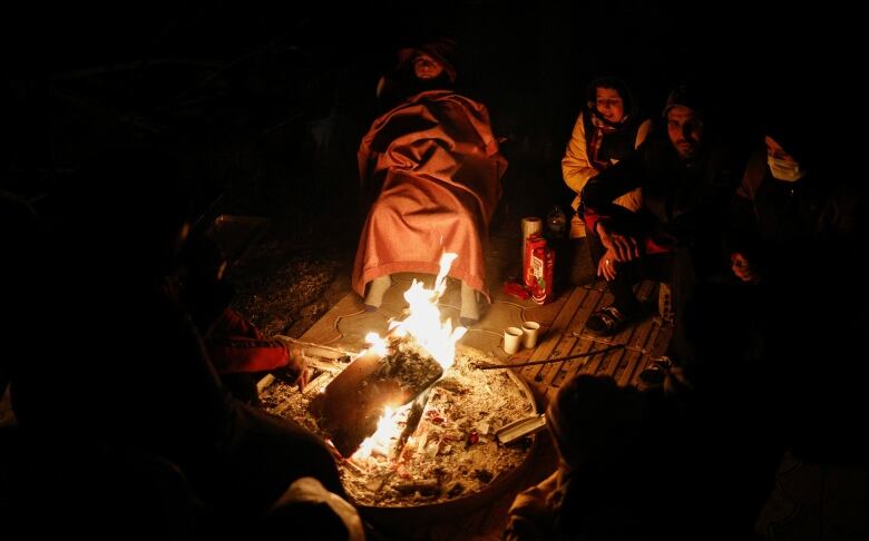 People sit around a small fire at night.