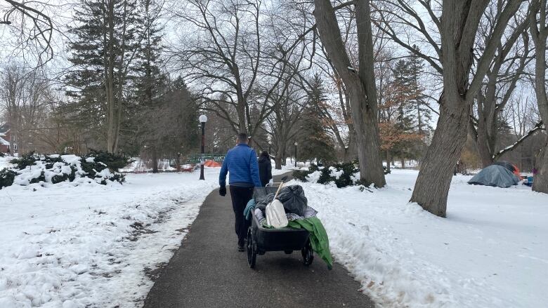 man pulls wagon full of various items on a sidewalk with snow on either side of him