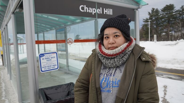 A woman stands in front of a bus shelter.