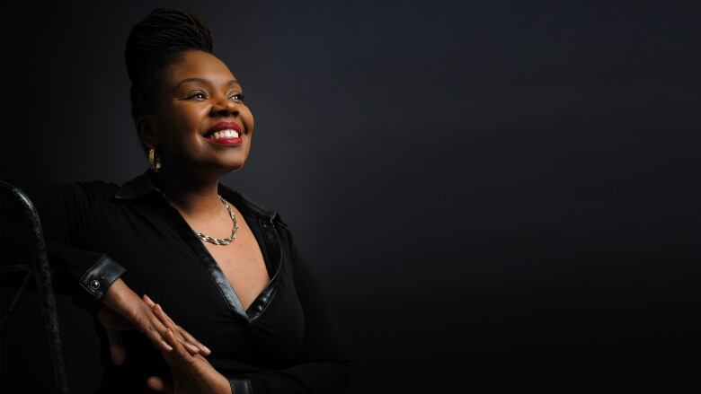 A Black woman in a leather-trimmed black top smiles widely.