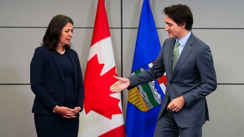 Alberta Premier Danielle Smith looks down at the hand of Prime Minister Justin Trudeau as he extends his hand for a handshake.