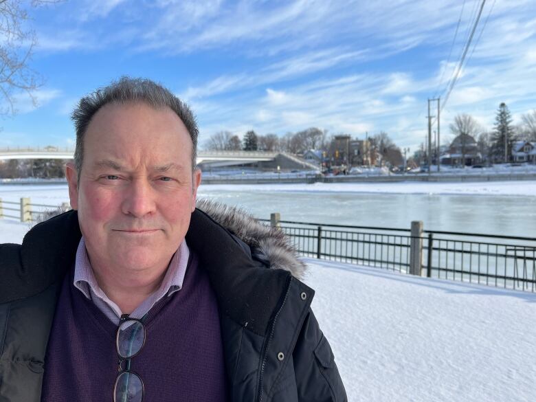 A man stands in an open coat in front of the Rideau Canal in winter.