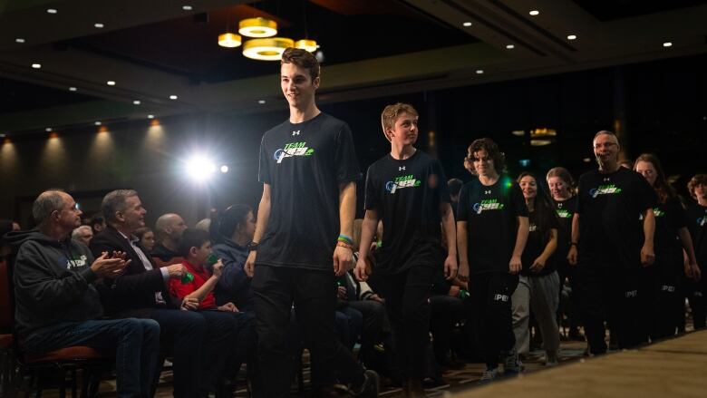 A group of young men walk past an audience. They're wearing Team P.E.I. t-shirts. 