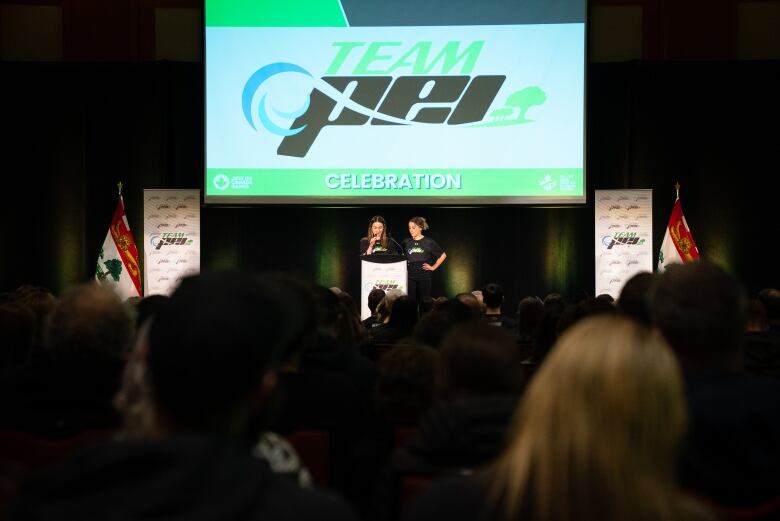 Two girls stand in front of a podium on a stage. 