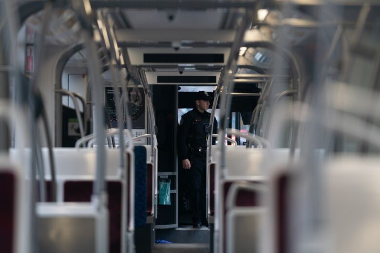 A man in a police uniform stands at the front of an empty streetcar. 