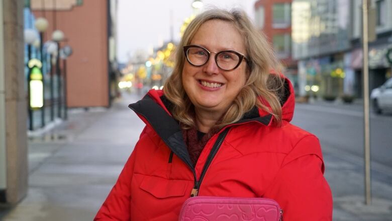 A woman wearing glasses and a bright red jacket smiles for a photo.