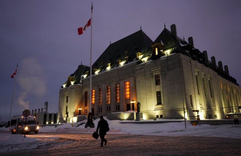 Someone walks outside a national court building in dim light, either dawn or dusk.