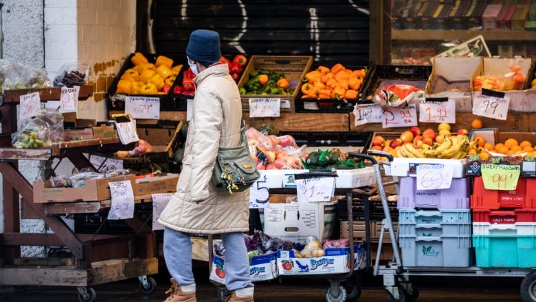 A person in a winter coat walks past a fruit stand.