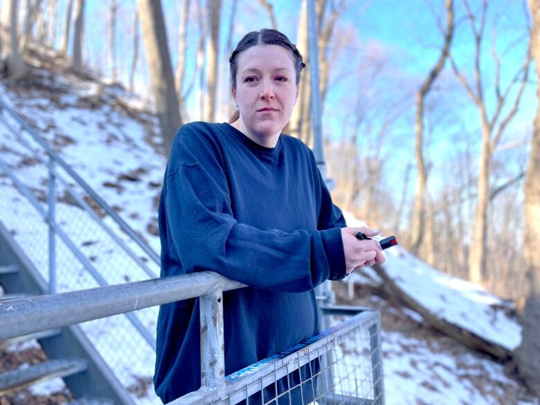 A woman in workout clothes stands at a railing on a set of outdoor stairs. There's snow on the ground and trees behind her.