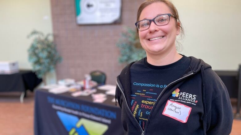 A smiling woman stands in front of a table holding pamphlets.