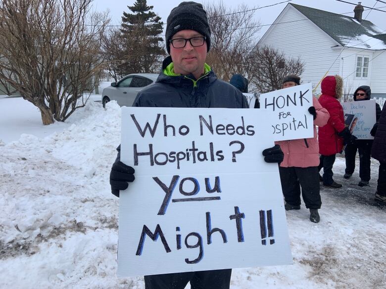 A person stands outside in the snow holding a sign saying 