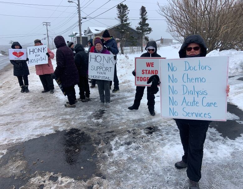 Several people stand outside holding signs. The closest sign says 