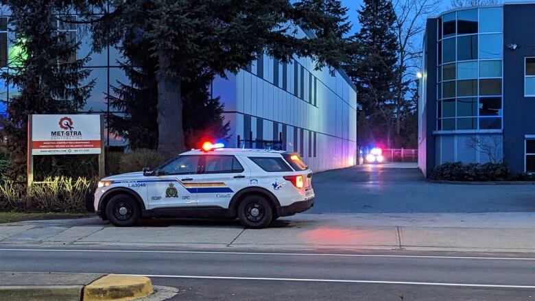 Two SUVs in RCMP livery are parked in an industrial area with their lights flashing.