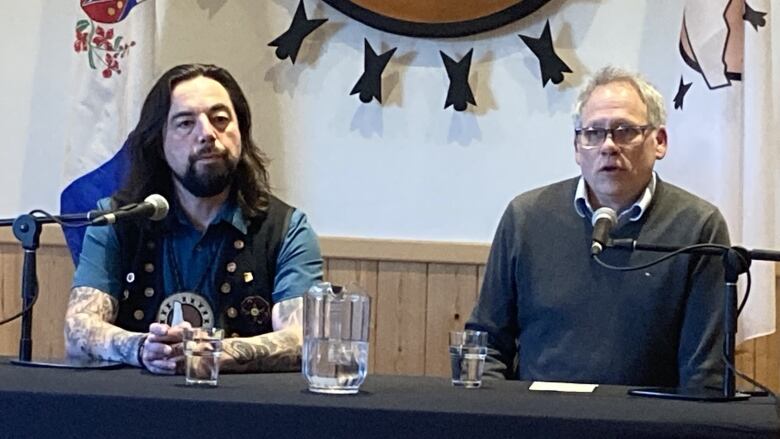 Two men at table, microphones, jug of water.