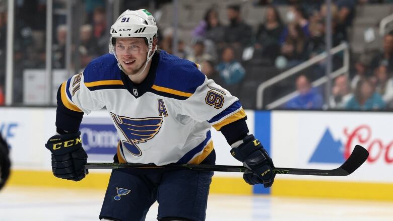 A hockey player holds his stick across his waist and smiles.