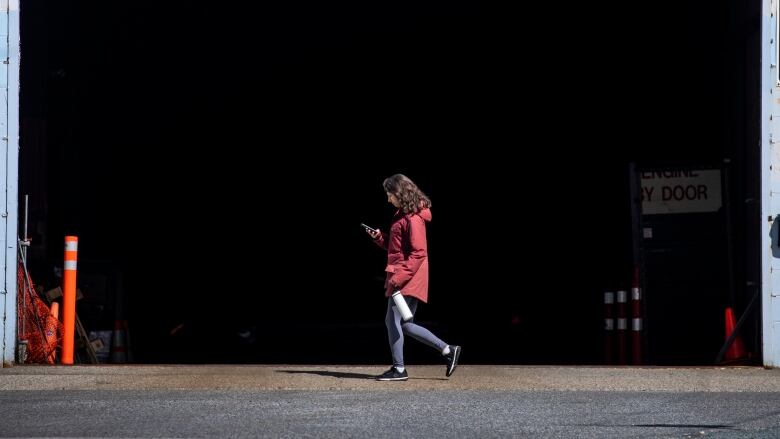 A woman in a red rain coat walks by a loading bay door.