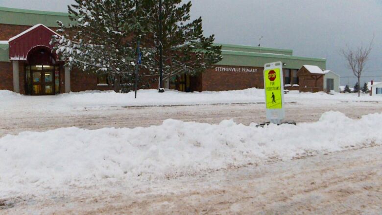 A brick building sits in the distance, with a tree and crossing sign in the foreground. Snow is on the ground.