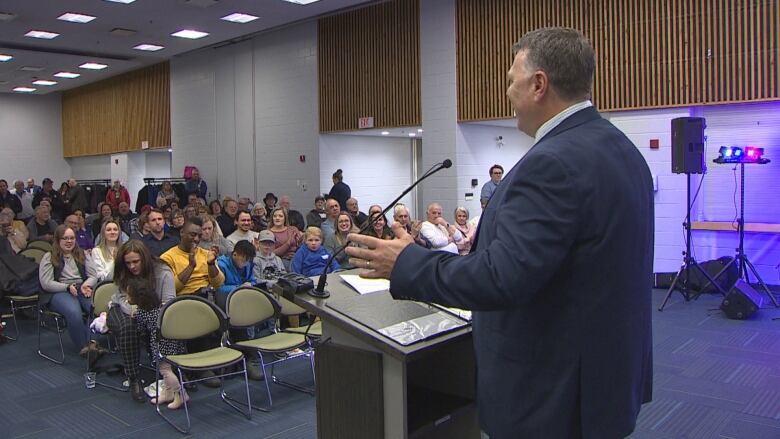 Premier Dennis King at a podium facing a crowd of people smiling and clapping.