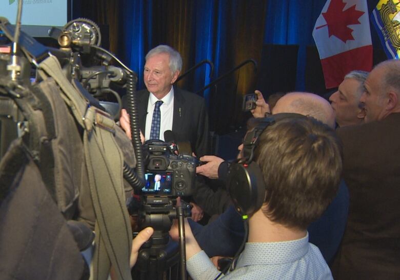 A man is surrounded by journalists holding microphones or cameras. 