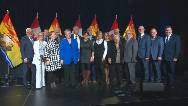 A large group of people pose on stage in front of New Brunswick flags.