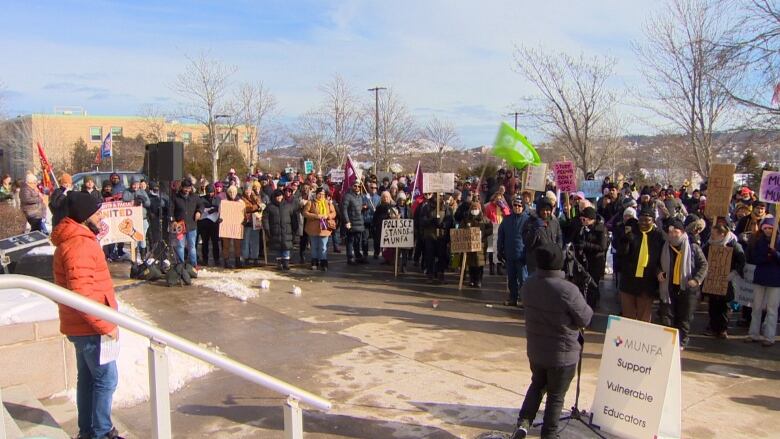 A large group of people holding strike posters stand at the bottom of a staircase. 