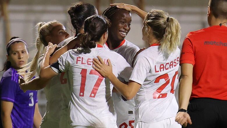 Women's soccer play pats teammate on head with right hand during a celebration with another player.