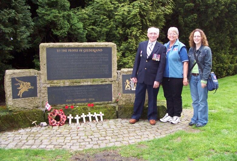 An elderly man and two women stand next to a war memorial.