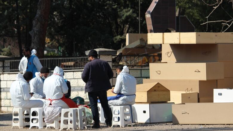 A group of workers sit next to a stack of wooden coffins.