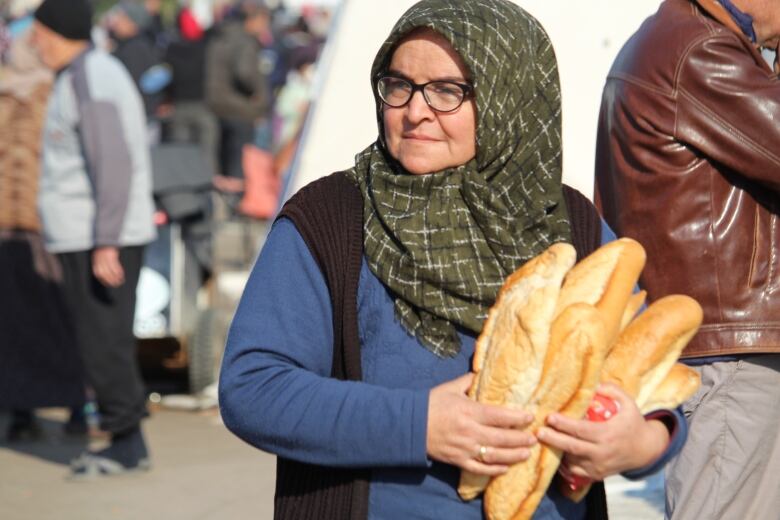 A woman clutches several loaves of bread to her chest.