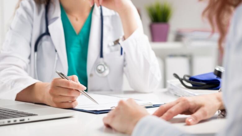 Two doctors, one with a stethoscope around her neck, have a medical discussion while looking at paperwork.