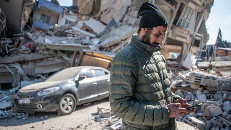 A man looks at his phone in a street destroyed by an earthquake in Turkey.