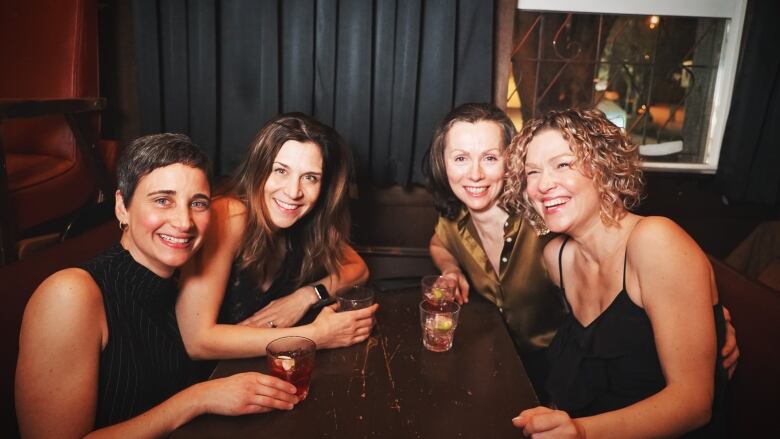 A group of white women smile for a picture while sitting at a table in a bar.