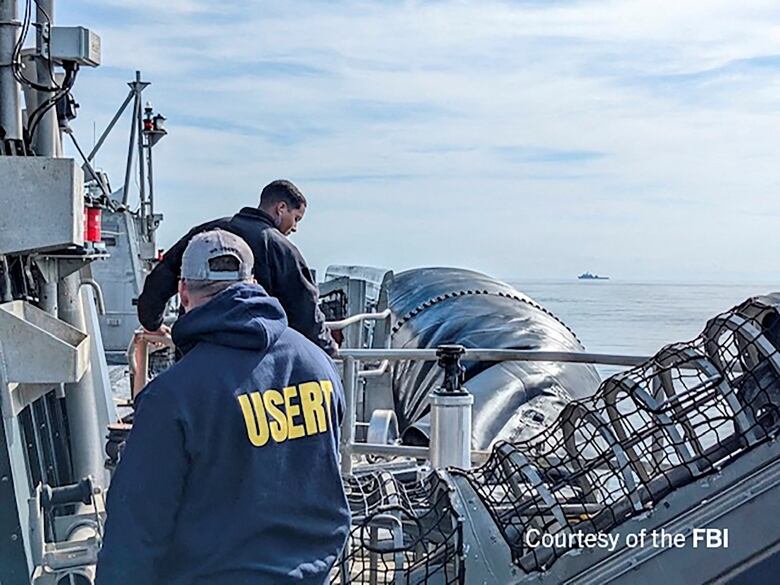 Two men in jackets are seen onboard a ship on a body of water.