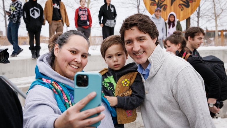 Smiling woman, child and Justin Trudeau take a selfie.