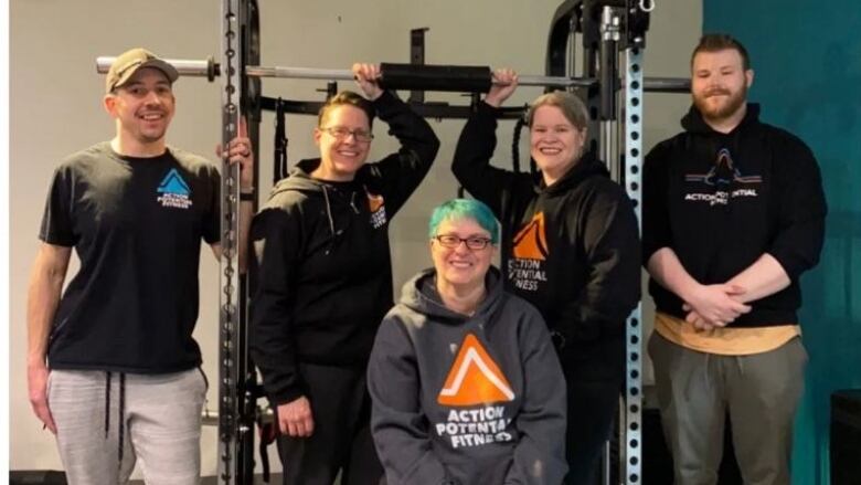 Five trainers stand smiling in front of a squat rack machine.