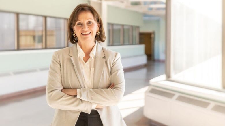 A portrait of a smiling woman with her arms crossed in a brightly lit hallway.