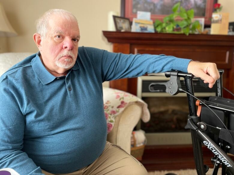 Man with white hair wearing aqua blue long sleeve shirt sits, with one hand on walker.