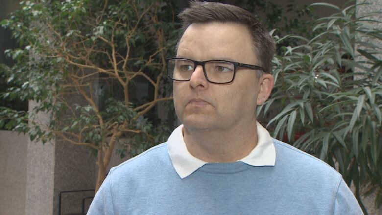 A man with glasses stands in front of plants.