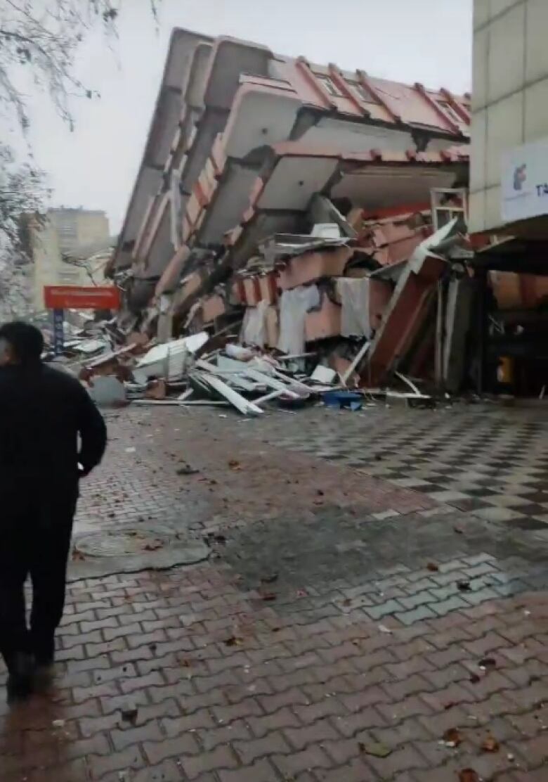 A pancaked building lying on it side is seen at the end of a cobbled street.