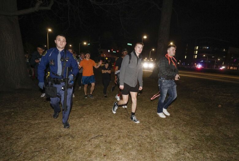 A man in a police uniform and several others are seen walking on the ground at night.